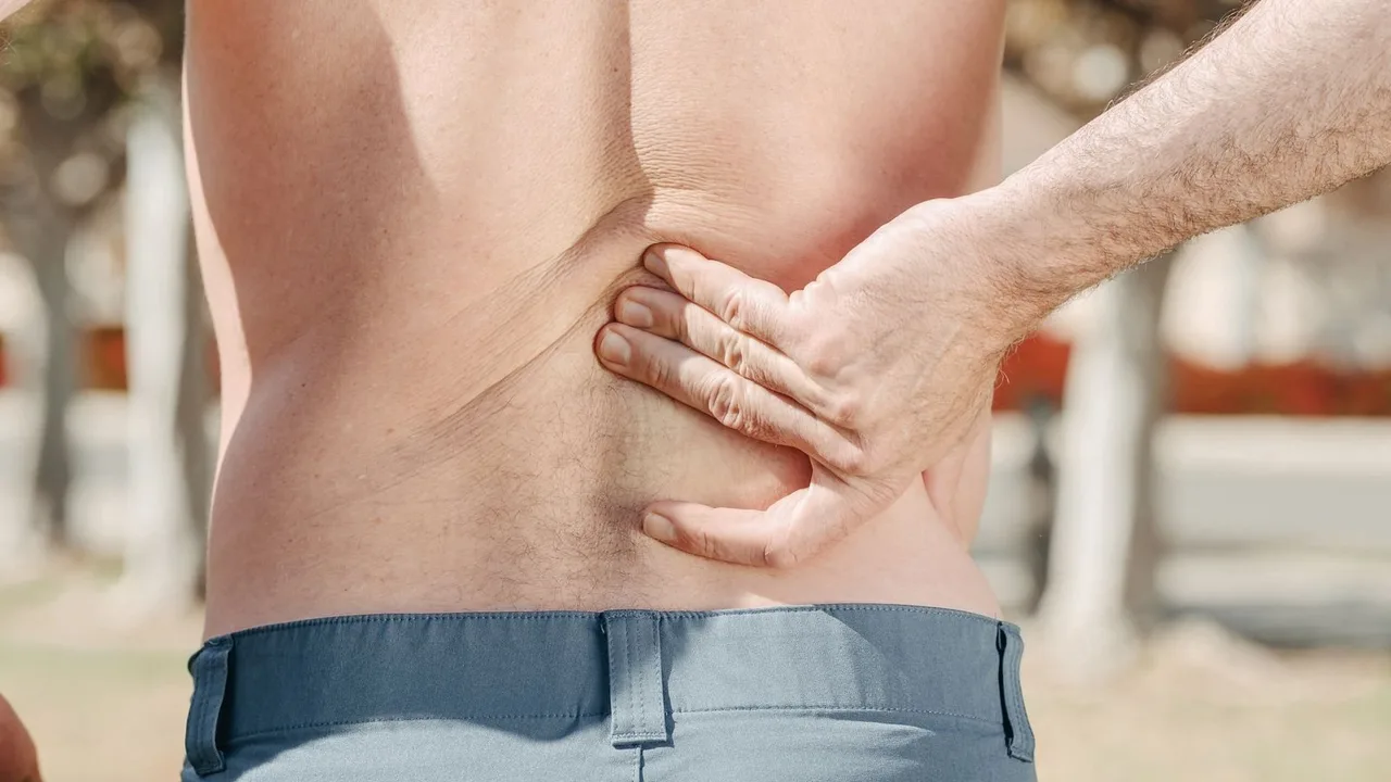 Homem com a mão na parte de baixo das costas, sinal de dor lombar.