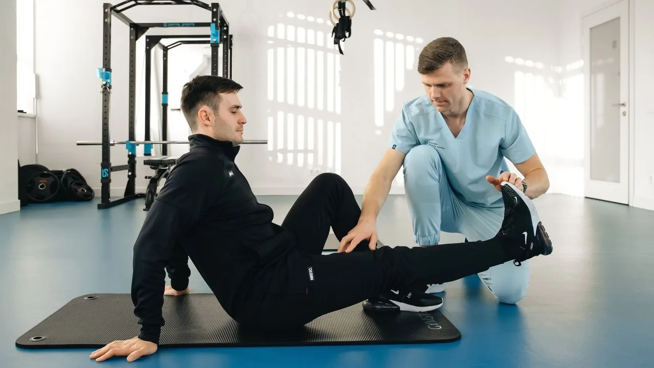 Fisioterapeuta orientando um paciente num exercício de perna sobre o tapete.