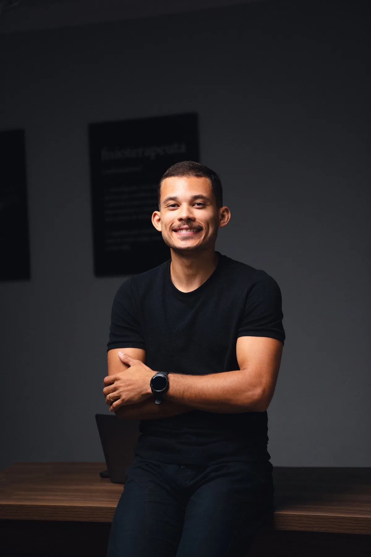Marlon Torres de camiseta preta, sentado na beira da mesa do consultório